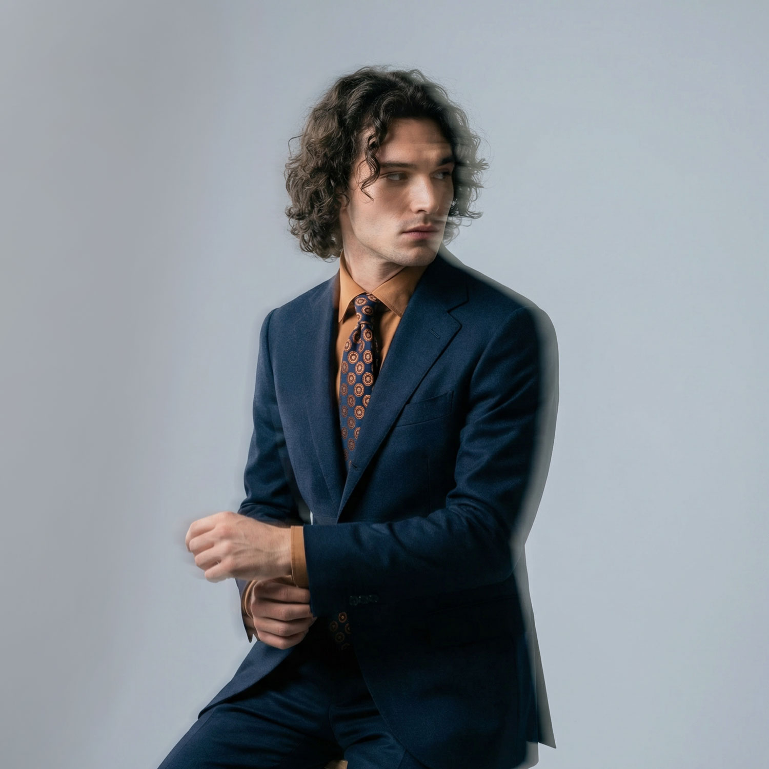 Man in navy tailored suit with patterned tie adjusting cuff in studio
